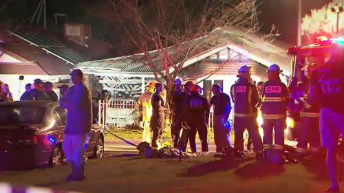 Neighbours and firefighters fill the street where a woman died in a house fire overnight. (Image: 9NEWS)