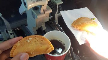 Two pilots drinking coffee and eating in their cockpit.