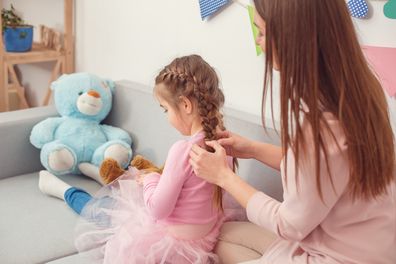 Young mother and little daughter together weekend at home sitting on sofa mom making hairstile for daughter