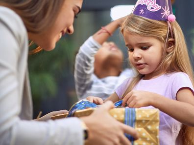 little girl unwrapping birthday present from young adult female brunette