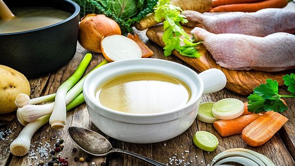 Bowl of stock surrounded by vegetables.