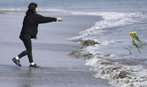 A man throws flower to the sea in tribute to the victims in the 2011 earthquake and tsunami in Arahama area, Sendai city, northern Japan, on Saturday, March 11, 2023. 