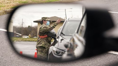 A National Guard soldier directing drivers is reflected in the mirror of a car waiting in a COVID-19 vaccination line  in Shelbyville, Tennessee.