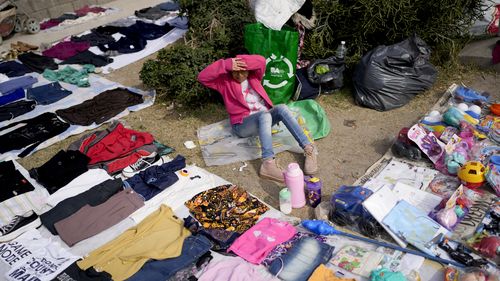 Una commessa siede circondata dai suoi vestiti usati esposti in un mercato dove le persone possono acquistare o barattare merci nella periferia di Buenos Aires, in Argentina.