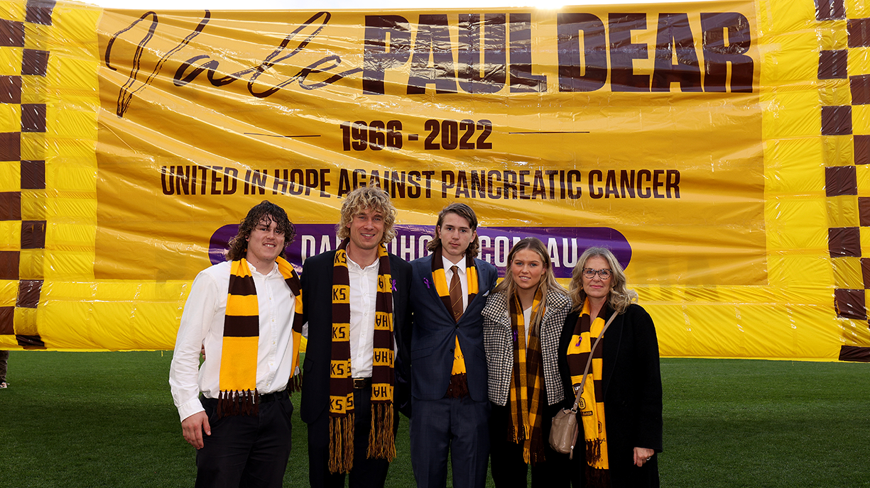 The family of late Paul Dear pose for a photo in front of the Hawks&#x27; banner ahead of their round 18 match in 2022.