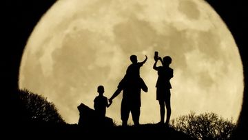 A family stand with the full moon known as the &quot;Sturgeon Moon&quot;