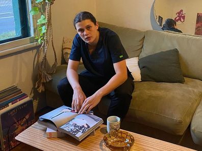 AFLW player Nell Morris-Dalton sitting at home in her nurse scrubs.