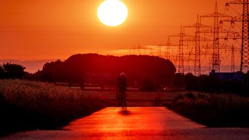 A man rides his bike on a small road with a sunset in the distance