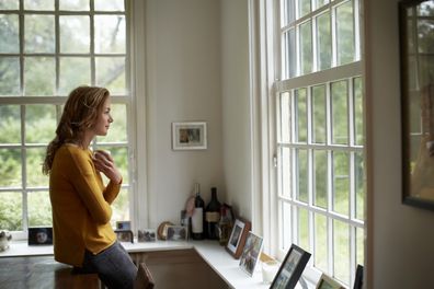 woman looking out window. woman enjoying cup of coffee. woman at home