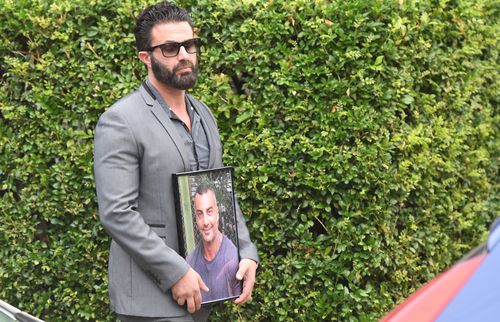A mourner arrives carrying a framed photograph of Mick Hawi (AAP).