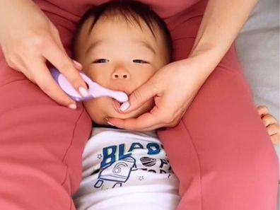 Baby being restrained between parents legs to brush his teeth.