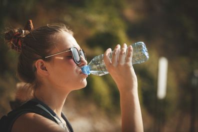 Side view of young woman drinking water from a bottle on a hot summer day.