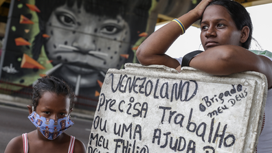 Melida Marquez, a 23-year-old Venezuelan woman holds a sign asking for job and help with her daughter Genesis, 6, at downtown Manaus on May 23 2020 in Manaus, Brazil. Melida arrived in Manaus a year ago, is pregnant with her fourth child and has no protective masks. 