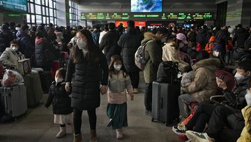 A woman and children wearing face masks walk by masked travelers wait at a departure hall to catch their trains at the West Railway Station in Beijing
