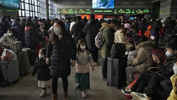 A woman and children wearing face masks walk by masked travelers wait at a departure hall to catch their trains at the West Railway Station in Beijing