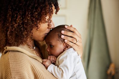 Close-up of a loving mother kissing her adorable little baby boy cradled in her arms at home