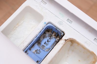 Dirty mouldy washing machine detergent and fabric conditioner dispenser drawer compartment close up. Mould, rust and limescale in washing machine tray. 