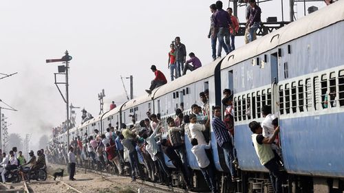 Commuters cling to the side of a packed train in New Delhi, India. Source: AAP
