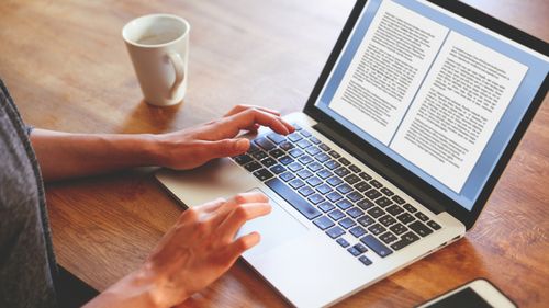 Imagem de alto ângulo de uma romancista ou blogueira, digitando no teclado do laptop enquanto toma uma xícara de café. Retro processado com cores vibrantes.