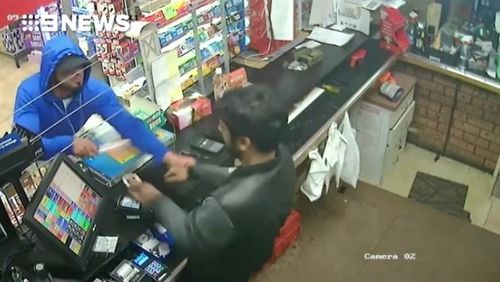 He grabs the cashier's hand while brandishing the knife.